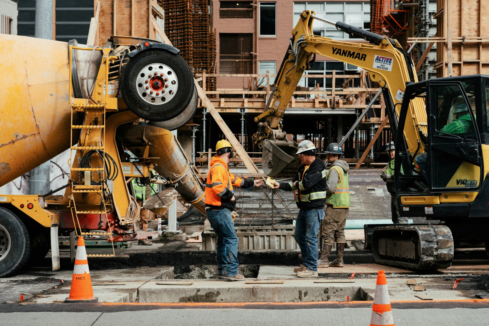 Construction workers coordinating beside concrete and excavation equipment on an active jobsite.